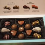 Geöffnete Pralinenschachtel mit verschiedenen Pralinen auf einem festlich gedeckten Tisch