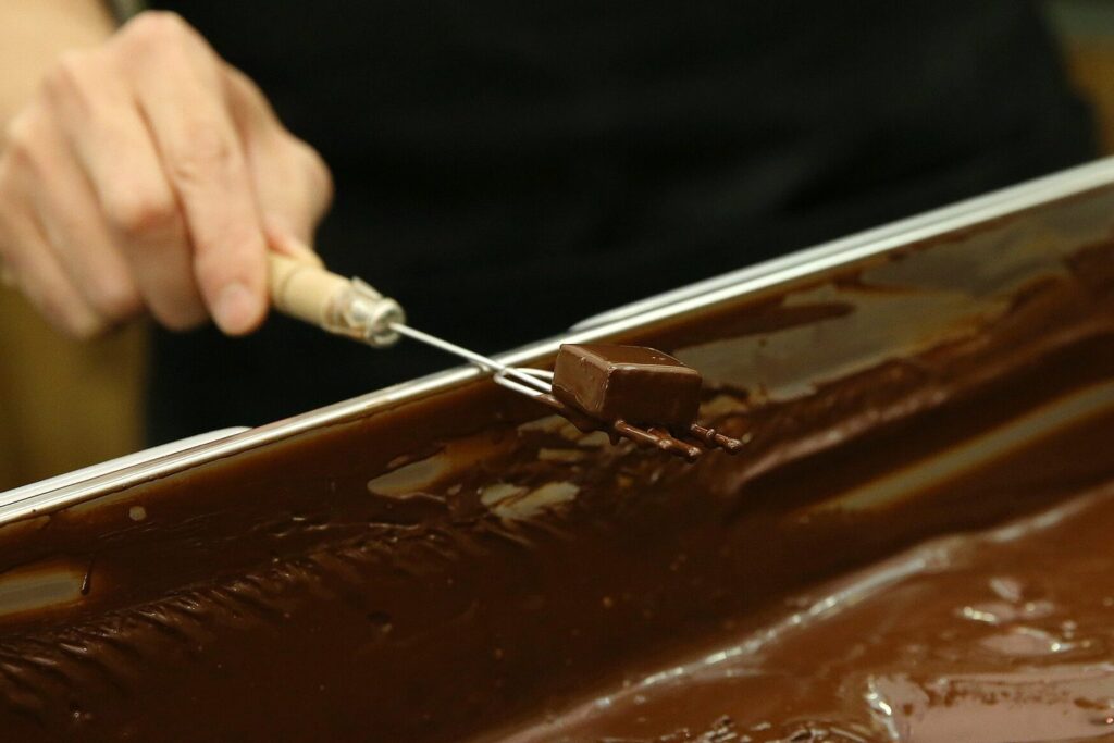Eine Praline wird mit einer Tauchgabel aus flüssiger Schokolade gehoben