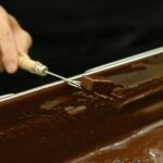 Eine Praline wird mit einer Tauchgabel aus flüssiger Schokolade gehoben