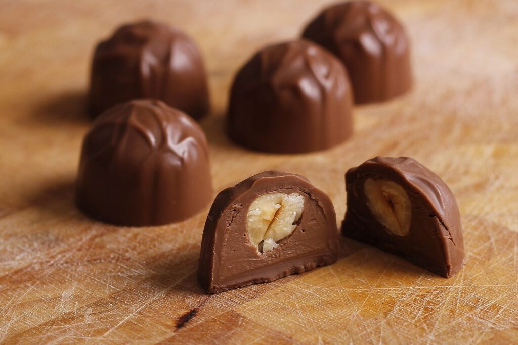 Gefüllte Nougat-Pralinen auf einem Holzbrett, eine davon aufgeschnitten