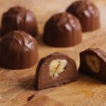 Gefüllte Nougat-Pralinen auf einem Holzbrett, eine davon aufgeschnitten