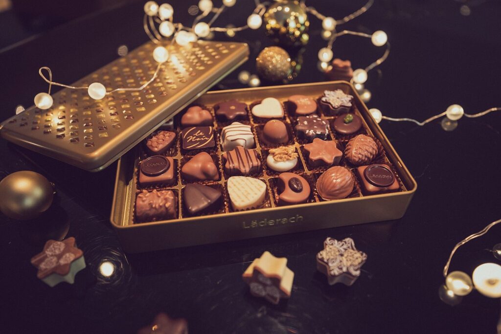 Geöffnete Weihnachtsdose mit Pralinés zwischen Kugeln und Lichterkette