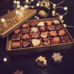Geöffnete Weihnachtsdose mit Pralinés zwischen Kugeln und Lichterkette